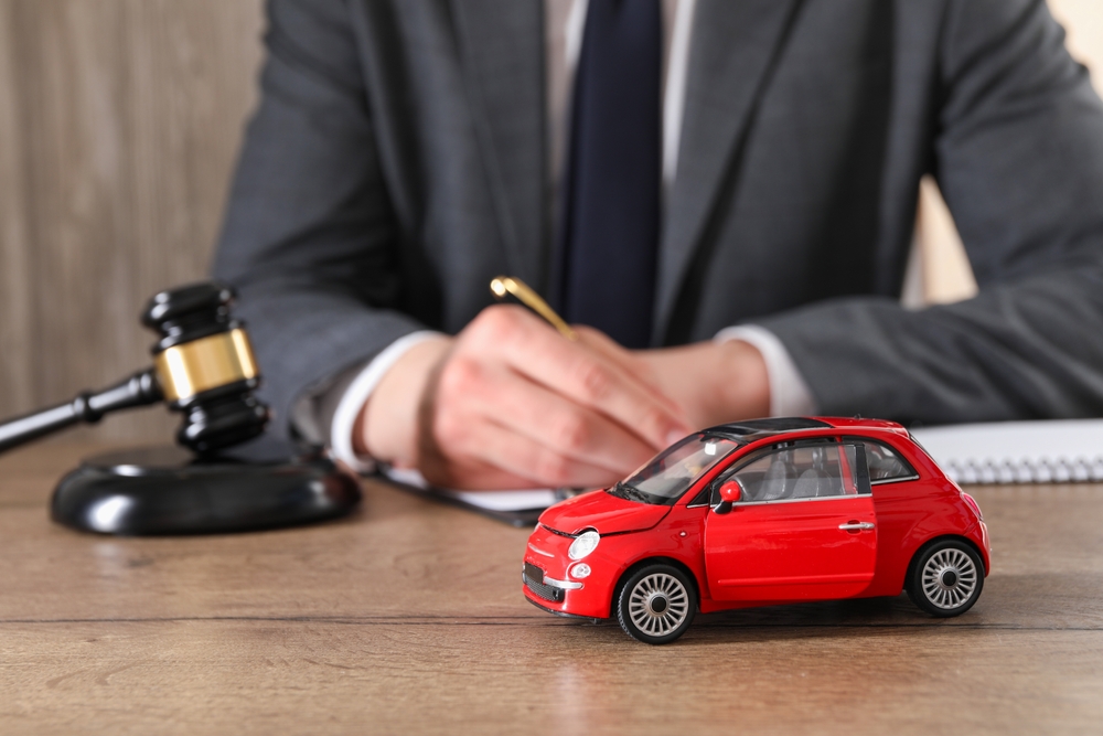 Auto accident law concept. Man working at a wooden desk indoors with focus on a toy car, symbolizing legal representation in vehicle collision cases.