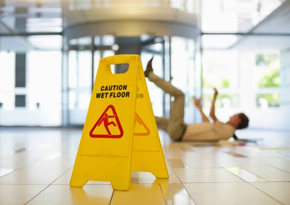 Businessman loses balance while slipping on a wet office floor, highlighting a workplace safety hazard.