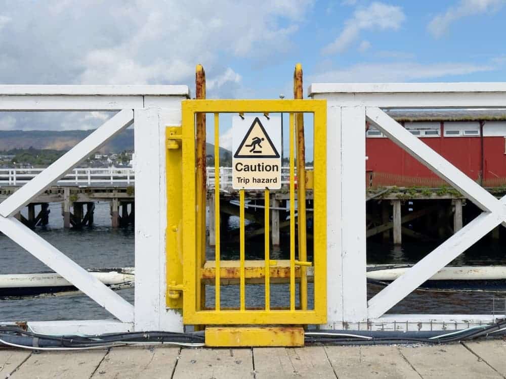 Trip hazard warning sign placed at the top of stairs leading down to the water from a harbor pier.