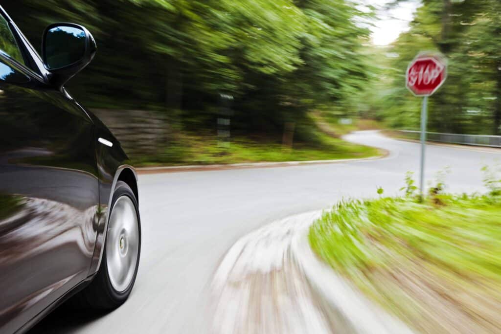 Car speeding on curved road near stop sign, illustrating reckless driving and potential traffic accident risk.